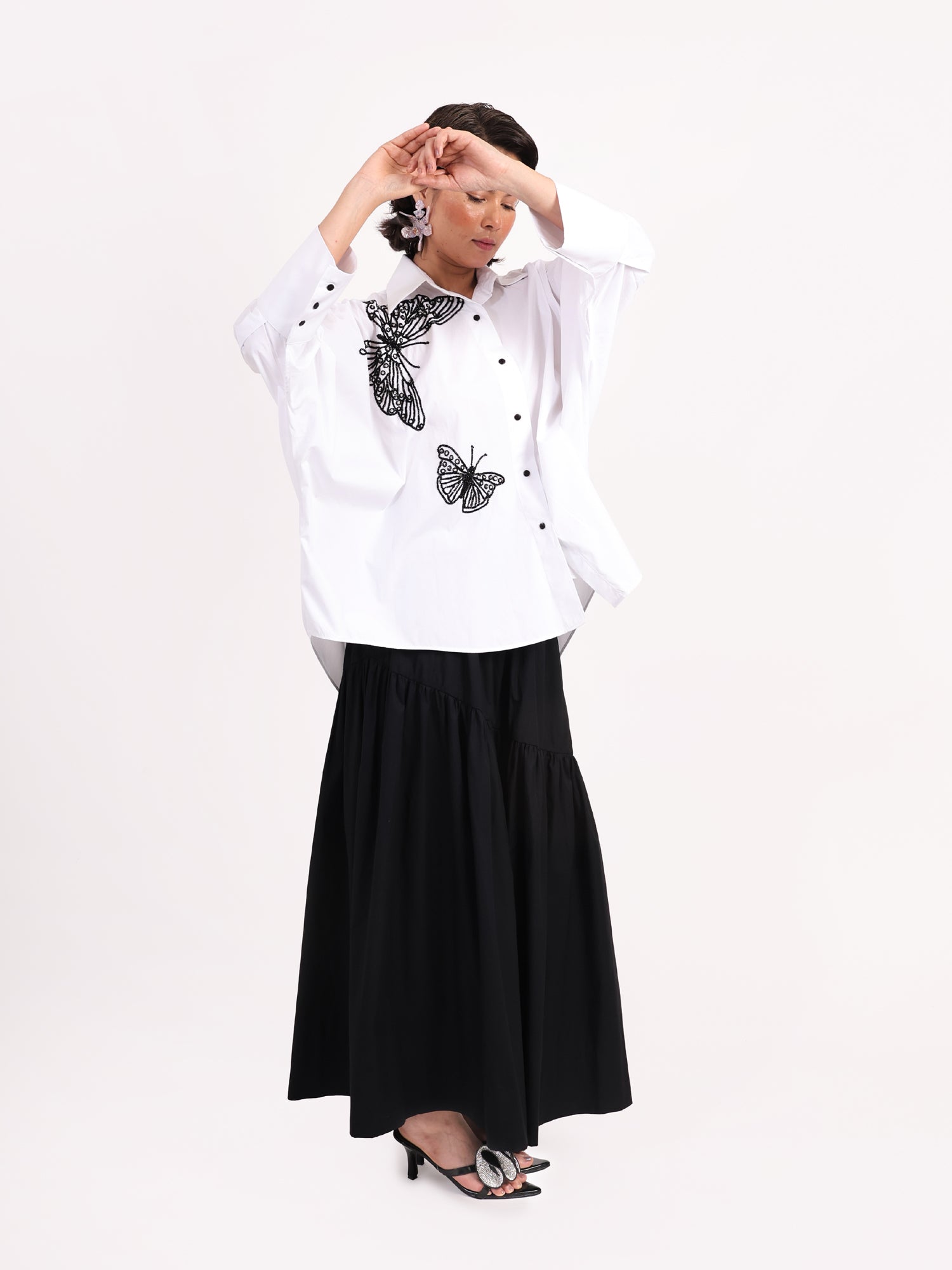 Woman wearing a white blouse with butterfly patterns and a black skirt on a white background