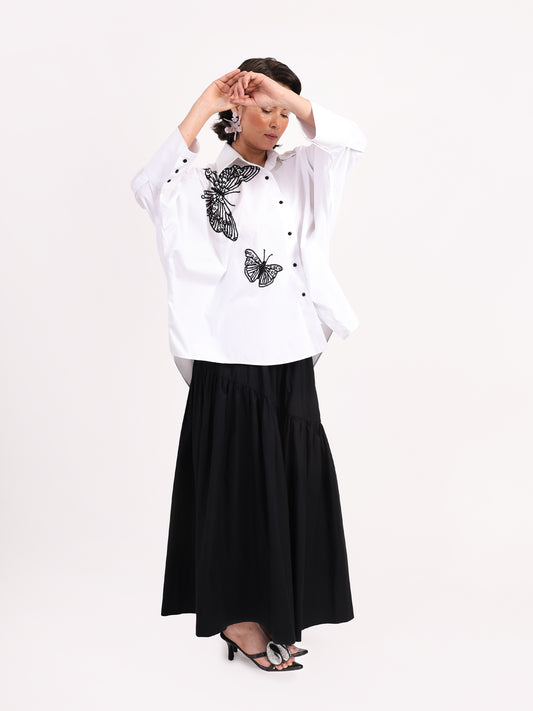 Woman wearing a white blouse with butterfly patterns and a black skirt on a white background